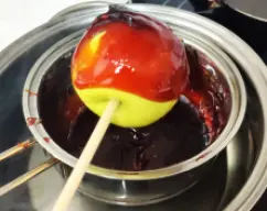 Step <p>Coja cada manzana por el palo y, con mucho cuidado para no quemarse, vaya bañándolas haciéndolas girar. Rellene el borde cerca del palo con una cucharilla. Deje escurrir y colóquelas en la bandeja sobre la silicona. Una vez frías, sirva a su conveniencia.</p> illustration