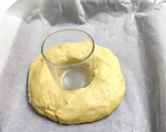 Step <p>Con la espátula, baje la masa hasta el fondo del vaso e inicie Amasar /1 min. Retire la masa del vaso sobre una superficie espolvoreada con harina y dele forma de bola. Introduzca los dedos en el centro y abra la masa de modo que el agujero central sea bastante grande e inserte un vaso en el agujero (quedará una corona o dos si decide hacer dos roscones más pequeños). Colóquela en la bandeja de horno preparada y deje reposar hasta que doble su volumen. Lave el vaso.</p> illustration