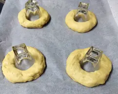 Step <p><u>Formado:</u></p><p>Para formar los roscones, introduzca los dedos en el centro y abra la masa de manera que el agujero central sea de aprox. 4 cm, yo lo hice con unos vasos de. Colóquelos en las bandejas de horno preparadas. Pinte con el huevo batido y deje reposar hasta que doble su volumen.</p> illustration