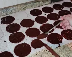 Step <p>Una vez derretido el chocolate, extienda una lámina de papel encerado o papel de horno sobre la mesa y dibuje circunferencias del tamaño que desee (un vaso le puede servir de guía fácilmente).</p> illustration