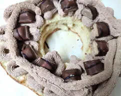 Step <p>Con un cuchillo de sierra, corte el roscón por la mitad transversalmente y rellénelo con la trufa. Distribuya 2 barritas de Kinder® Chocolate en trozos sobre la trufa (opcional) y vuelva a poner la parte superior del roscón.</p> illustration